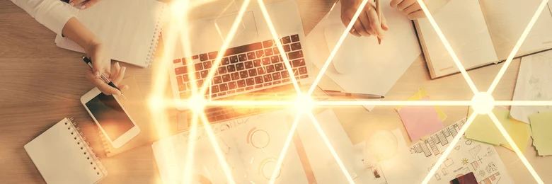 Zwei Personen sitzen an einem Tisch, auf dem verschiedenste Papiere, ein Laptop und ein Handy liegen.