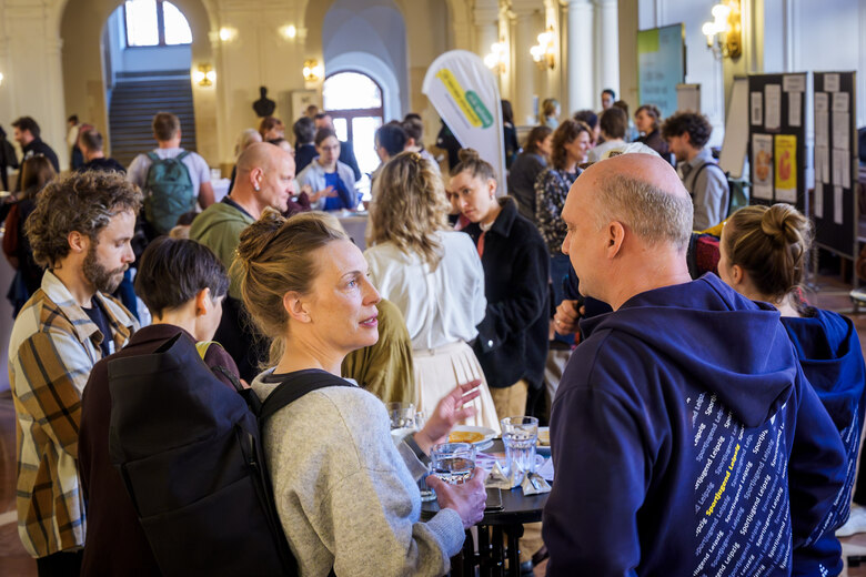 Blick in die Obere Wandelhalle des Rathauses, in der viele Personen um Stehtische stehen und miteinander sprechen.