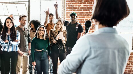Über die Schulter einer Person ist eine Gruppe von jungen Menschen zu sehen.