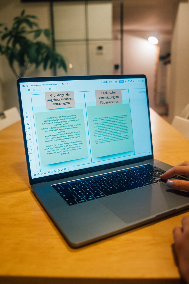 Auf einem Tisch steht ein Laptop, auf dem auf einer digitalen Pinnwand verschiedene Handlungsempfehlungen angezeigt werden.