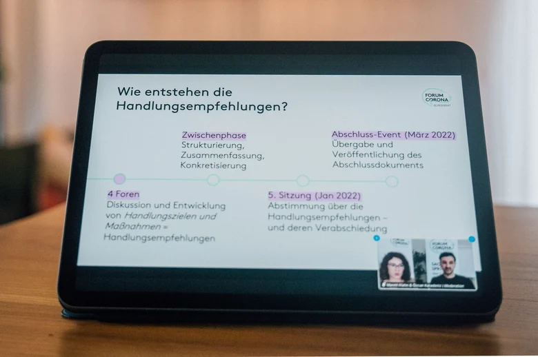 Auf einem Tisch steht ein Tablet, auf dem eine Präsentationsfolie zu sehen ist, auf der "Wie entstehen die Handlungsempfehlungen?" zu lesen ist.