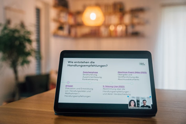 Auf einem Tisch steht ein Tablet, auf dem eine Präsentationsfolie mit dem Titel "Wie entstehen die Handlungsempfehlungen?" zu sehen ist.