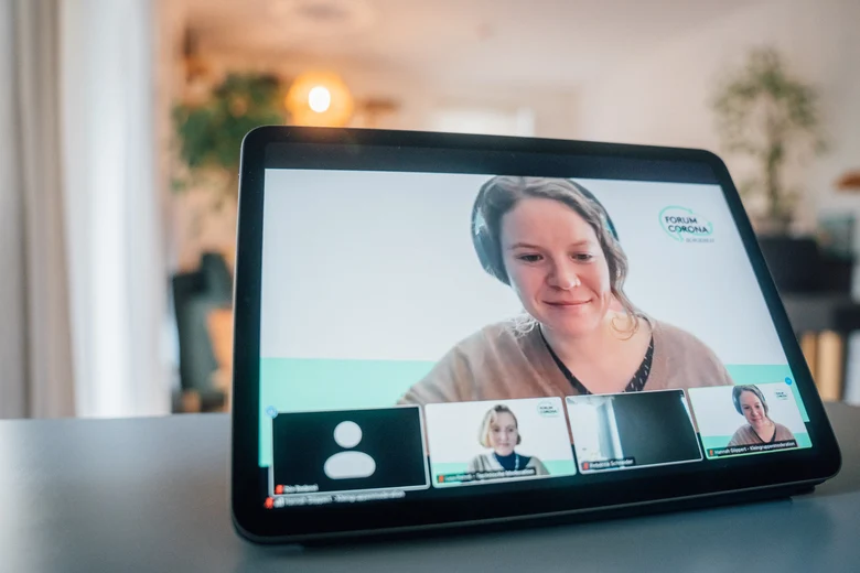 Auf einem Tisch steht ein Tablet, auf dem die Teilnehmenden der Videokonferenz zu sehen sind.