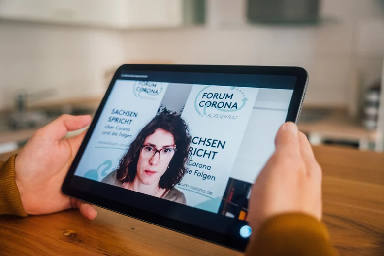 Eine Person hält ein Tablet in der Hand, auf dem das Video der Moderatorin Marett Klahn zu sehen ist.
