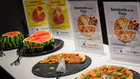 Melone und Pizza am Buffet mit Pizza- und Melonen-Plakaten im Hintergrund.