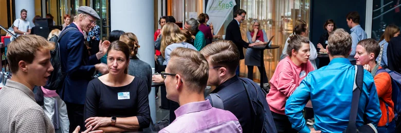 Viele Personen stehen in einem Foyer und unterhalten sich in kleineren Gruppen an Stehtischen.