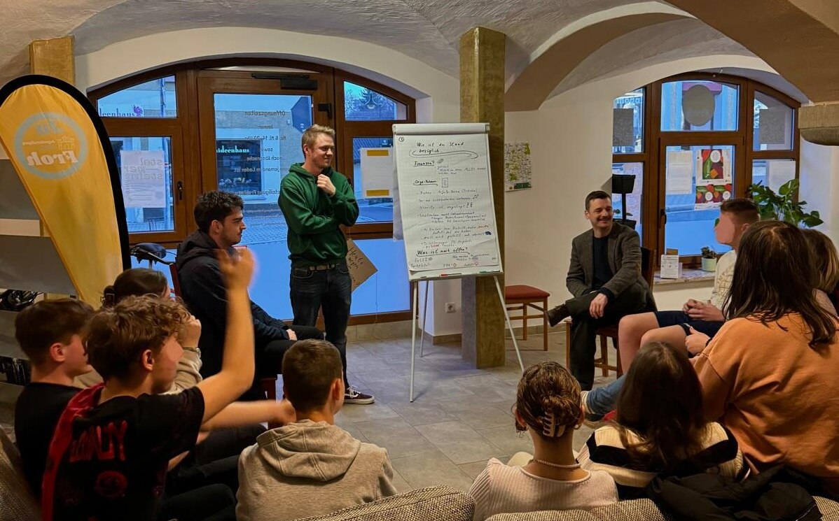 Jugendliche sitzen im Kreis zusammen und beraten sich, auf einem Flipchart stehen Notizen