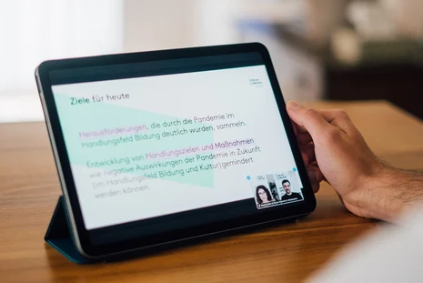 Themen des Bürgerrats Forum Corona Eine Person hält ein Tablet in der Hand, auf dem eine Präsentation zu sehen ist.