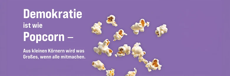 Vor einem lila Hintergrund sind mittig mehrere Popcornkörner zu sehen, daneben steht: Demokratie ist wie Popcorn - Aus kleinen Körnern wird was Großes, wenn alle mitmachen.